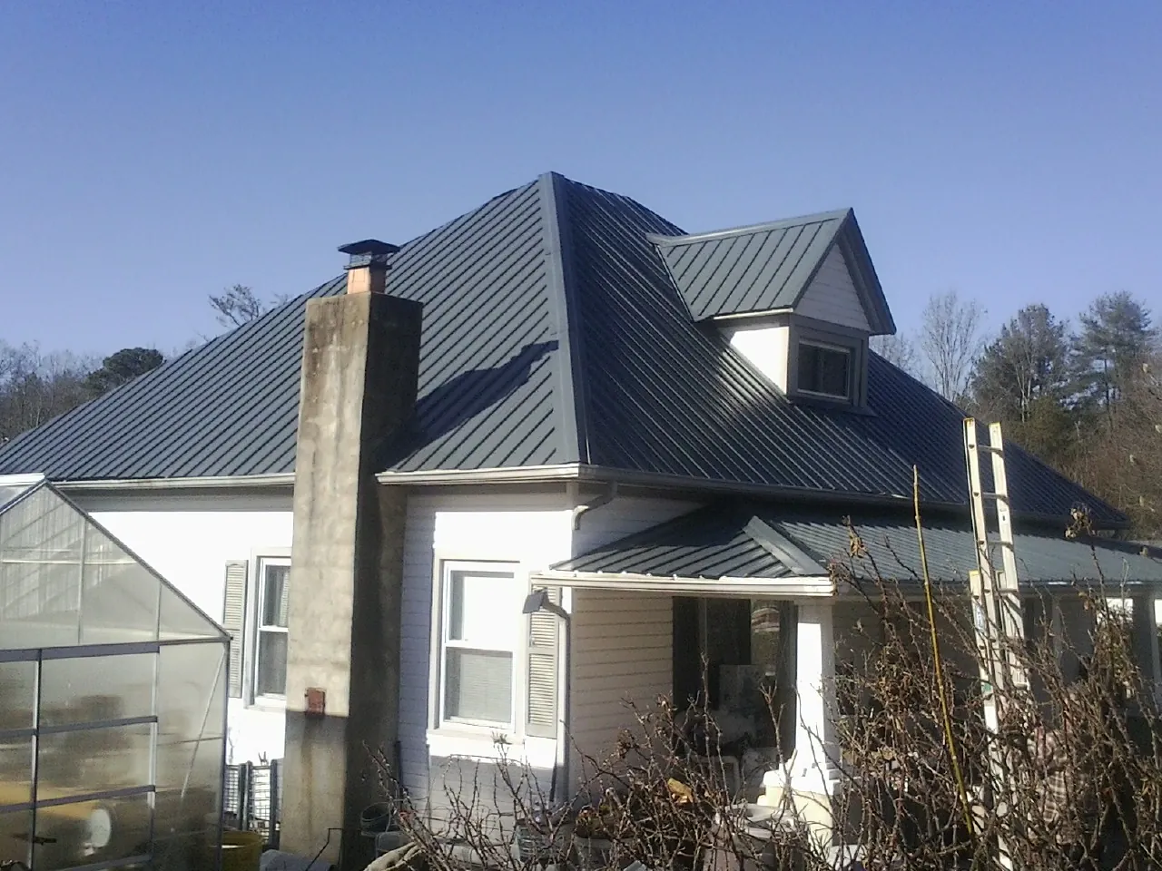Dark blue standing seam metal roof on a white farmhouse with dormer in Howey In The Hills