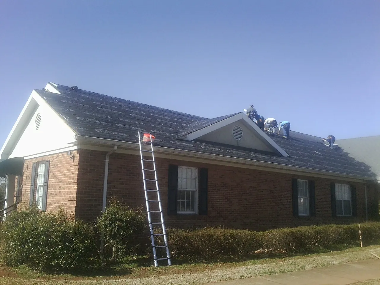Crew tearing shingles off a brick ranch roof with a ladder set — Emergency Roof Repair work by our crew in Howey In The Hills