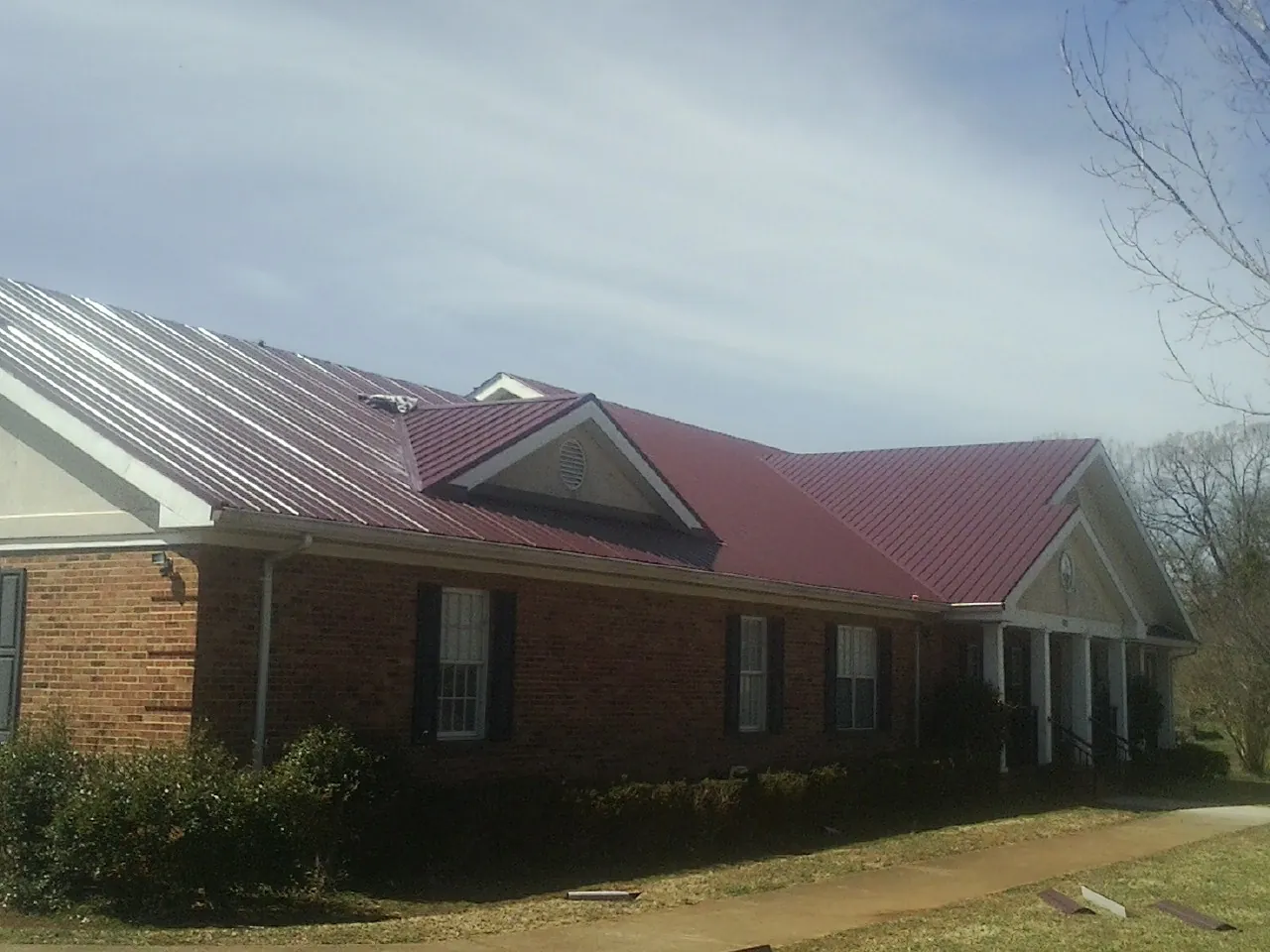 Red metal roof with gabled entries on a long brick building, from a Hail Damage Roof Repair job in Howey In The Hills