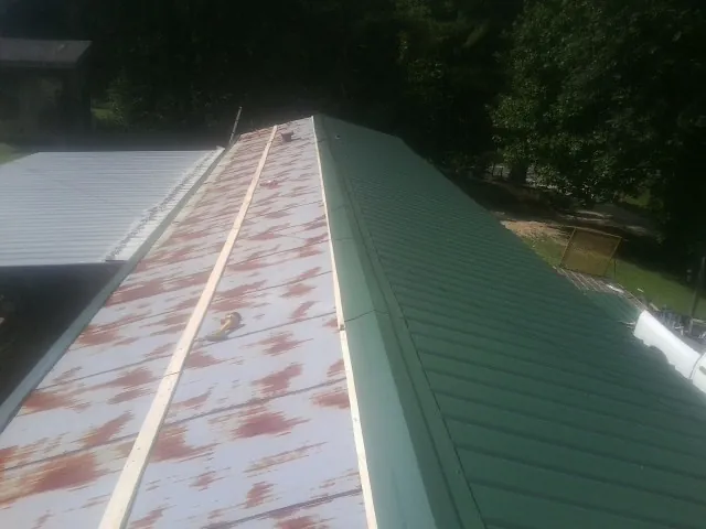 Old rusted panels beside newly installed green metal roofing — Wind Damage Roof Repair by Roofing Brothers in Howey In The Hills