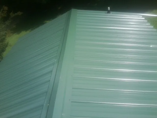 New green metal panels meeting at the ridge of a roof — Flat Roof Repair work by our crew in Howey In The Hills