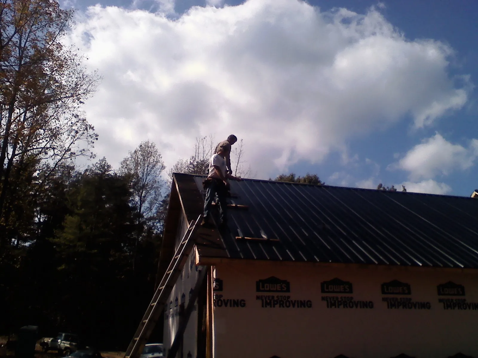 Roofer fastening dark metal panels high against a cloudy sky, from a Roof Inspection job in Howey In The Hills