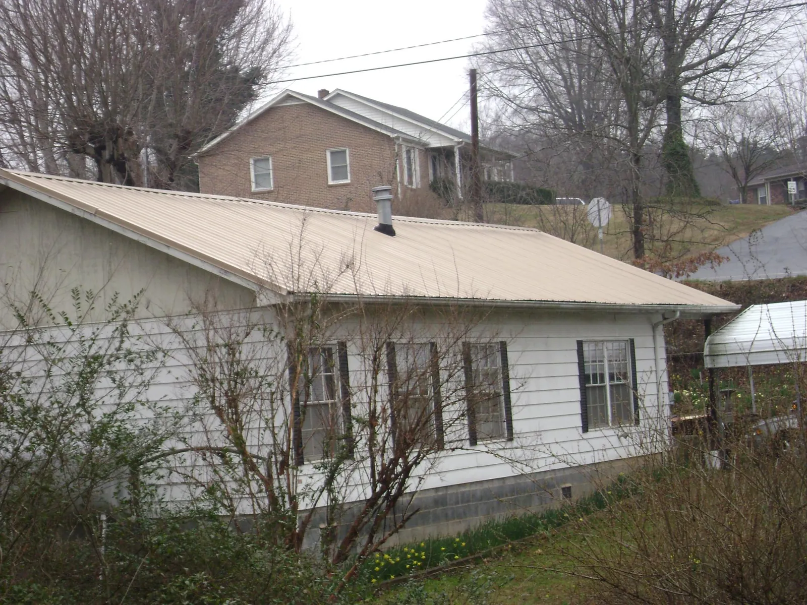 Tan metal roof on a white sided house set into a hillside — Commercial Roofing by Roofing Brothers in Howey In The Hills