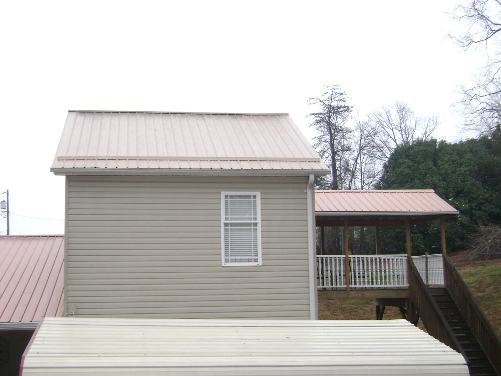 Tan metal roofs on a two story addition and attached porch, from a Roof Replacement job in Howey In The Hills